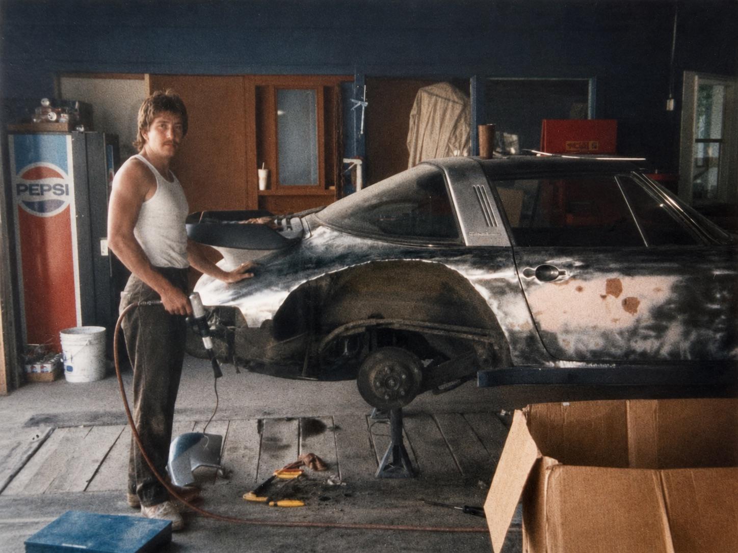 Rick Hummert in the early 1980s working on a stripped Porsche 924 in his original St. Louis shop, holding a sander with a Pepsi machine in the background